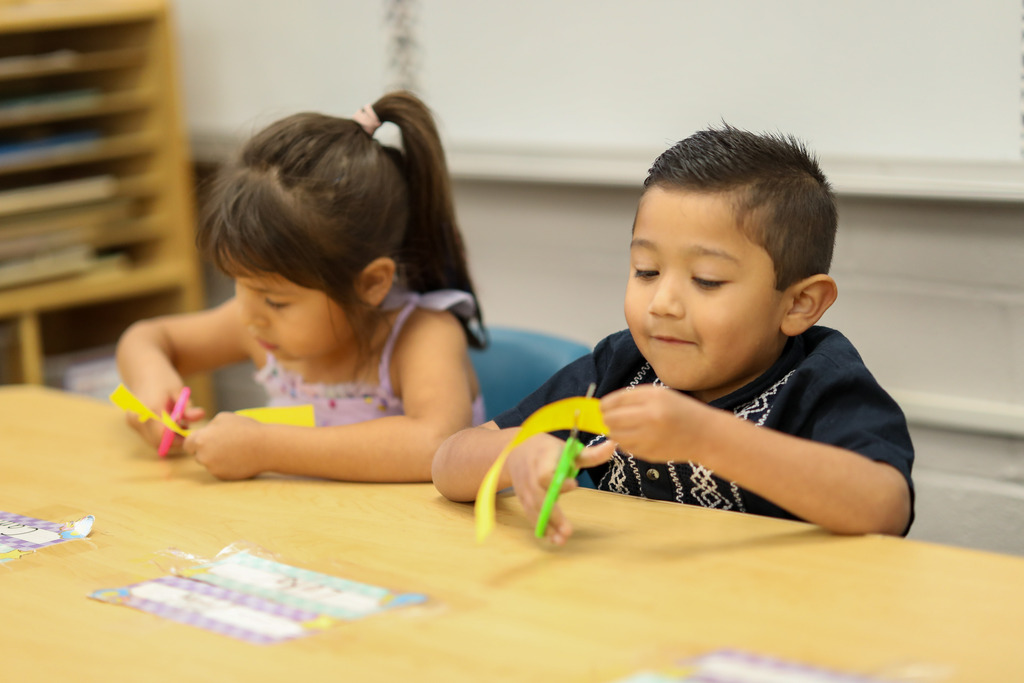 A boy and girl cut strips into pieces of paper.