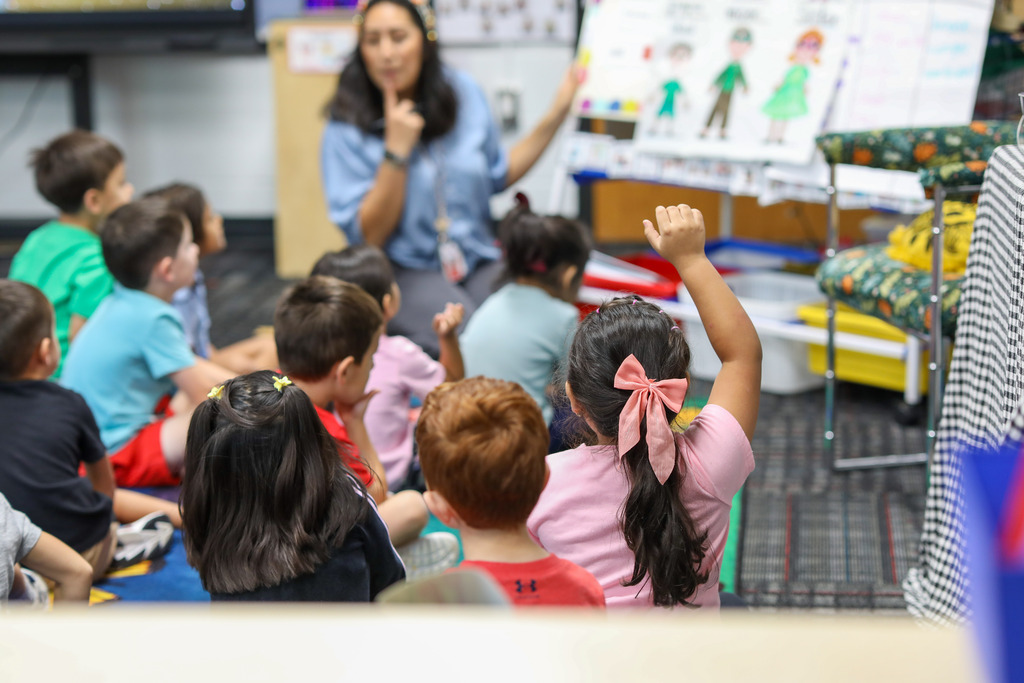 Students raise their hands while the teacher explains.