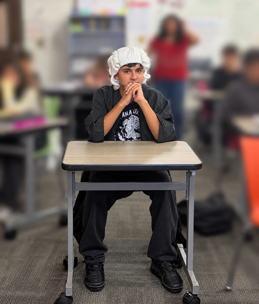 A student wearing a judge’s robe sits at the front of the classroom during a mock trial activity, listening to classmates present evidence and defend their arguments.