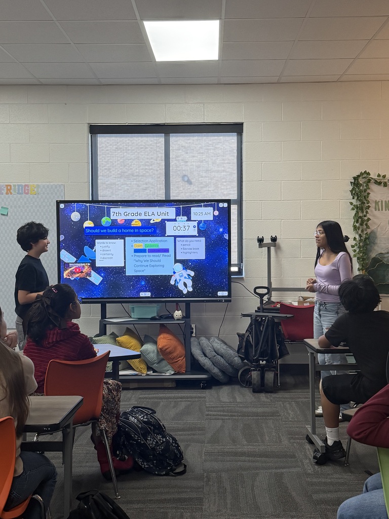 Two students stand at the front of the classroom presenting their case during a mock courtroom activity, using evidence and reasoning to support their argument.