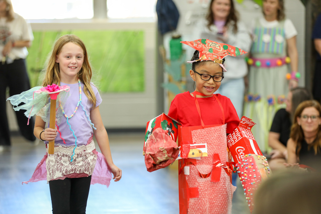 students smiling and walking in a runway fashion show using recycled materials