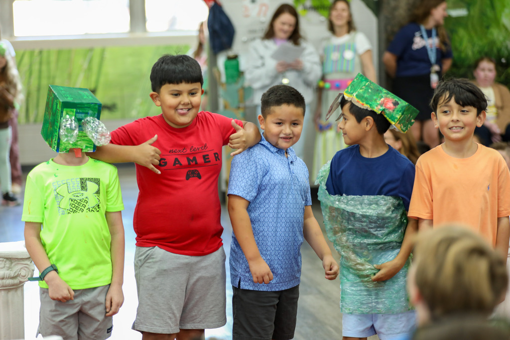 students smiling and posing in a runway fashion show using recycled materials