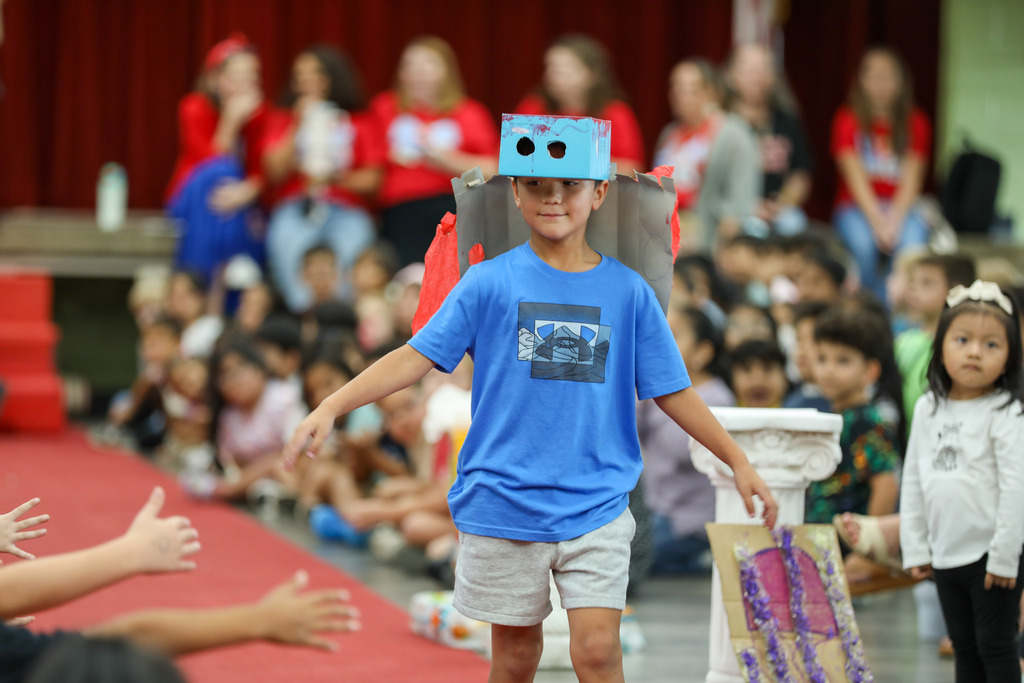 students smiling and walking in a runway fashion show using recycled materials
