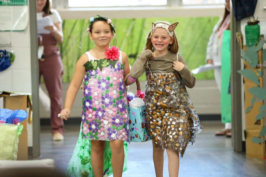 students smiling and walking in a runway fashion show using recycled materials