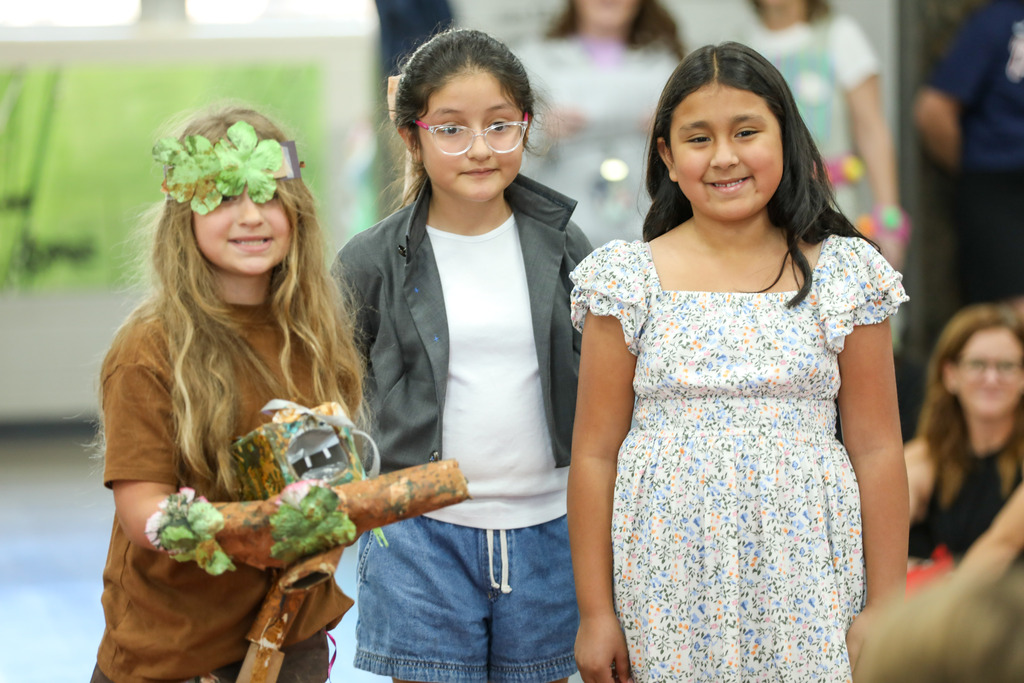 students smiling and posing in a runway fashion show using recycled materials