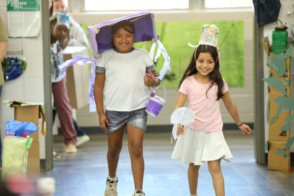 students smiling and walking in a runway fashion show using recycled materials