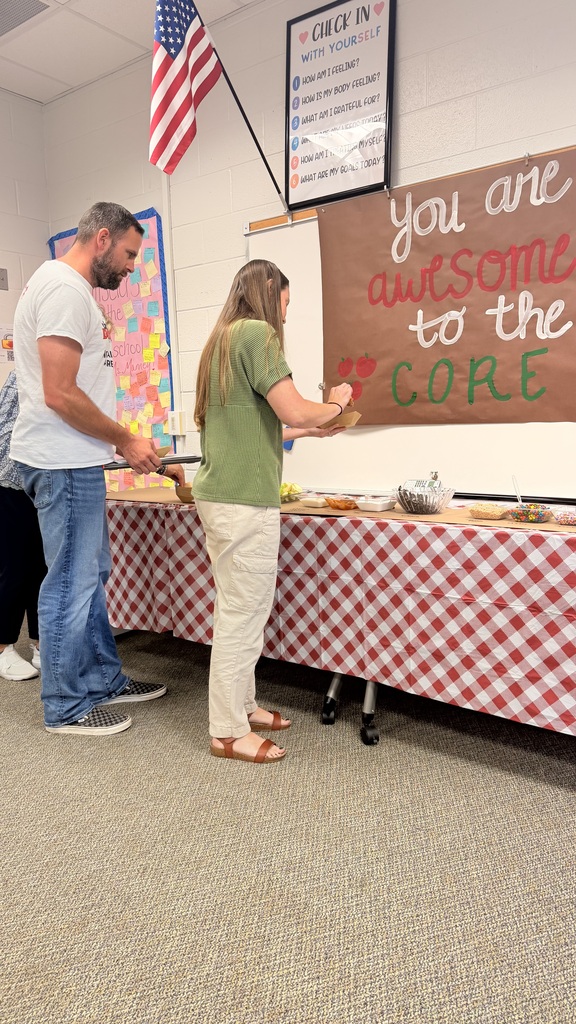 Two people standing at a table creating custom apple treat bowls under a sign that says "You are awesome to the CORE."