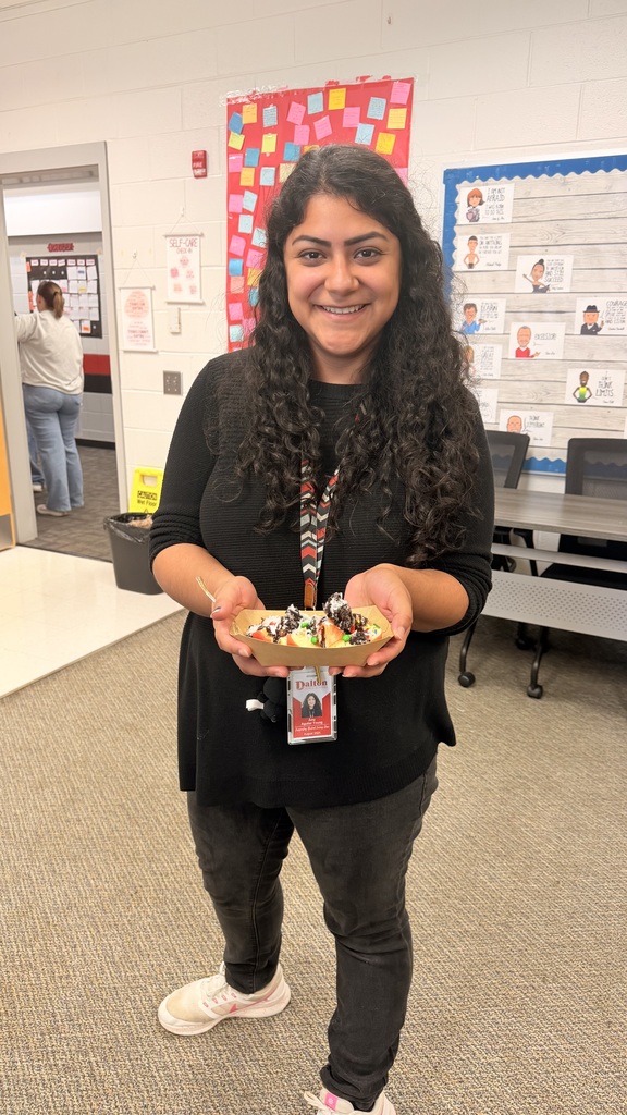 A smiling woman standing in an office holding a cardboard boat filled with loaded apple slices.