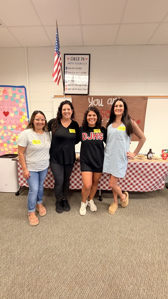 Four women standing together and smiling in front of a table set up with an apple bar and a sign reading "You are awesome to the CORE."