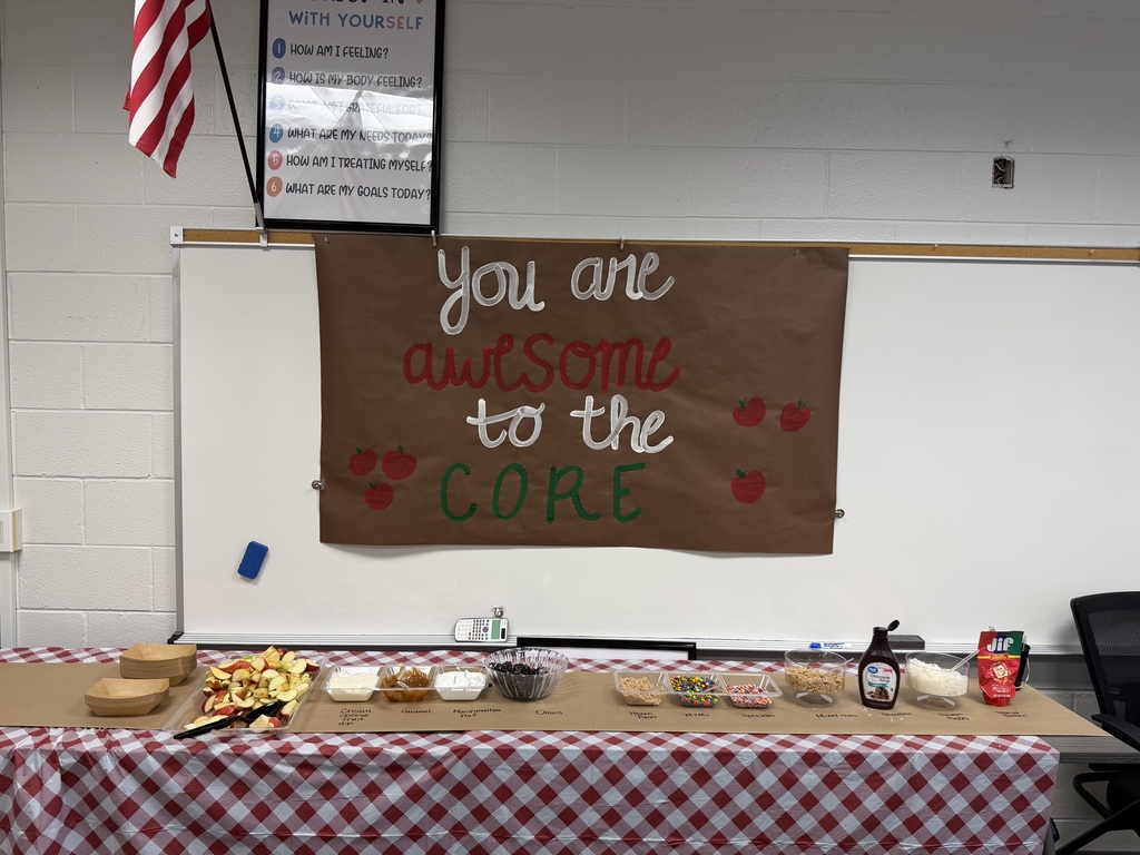 An apple bar setup on a table with a red-and-white checkered tablecloth, topped with sliced apples, dips, and various toppings beneath a sign that reads "You are awesome to the CORE."