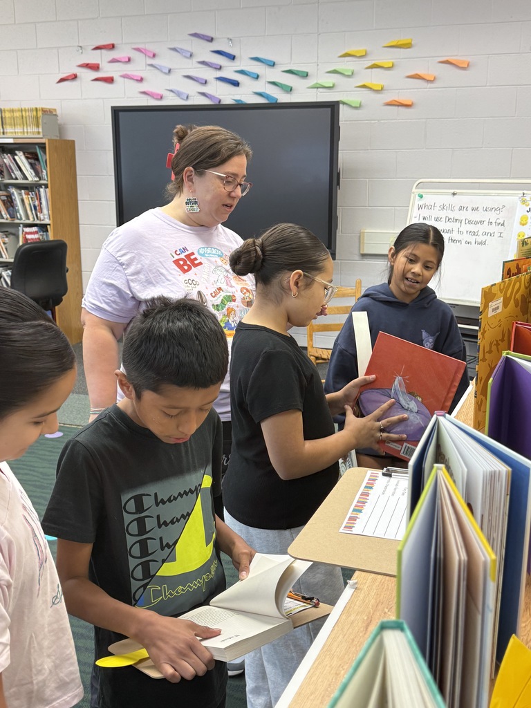 A teacher assisting students as they examine library books during a group lesson.