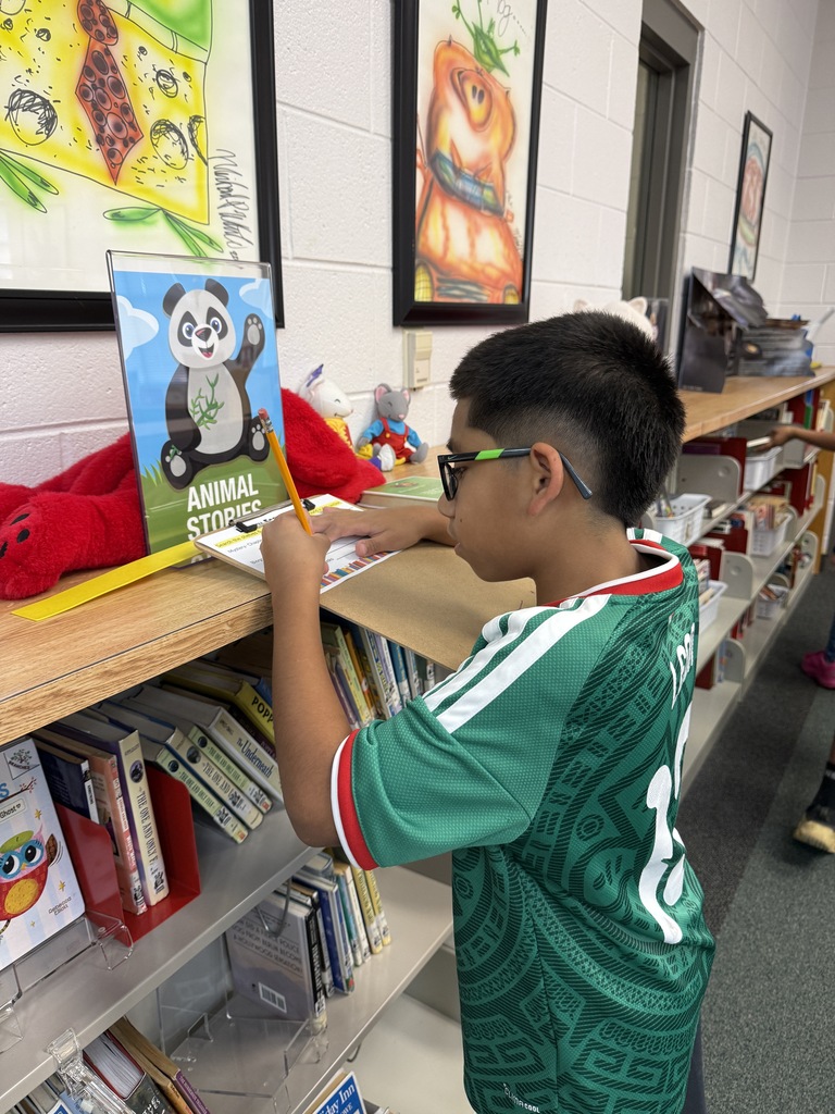A boy writing on a clipboard at a library shelf labeled "Animal Stories".