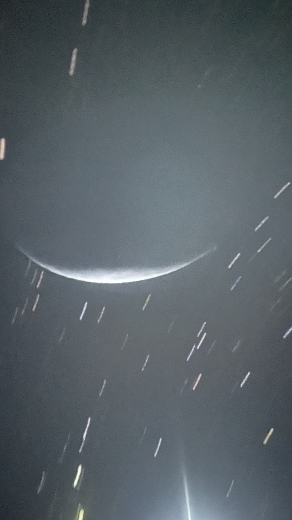Projection of a thin crescent moon surrounded by light trails and stars on a dark background inside a planetarium dome.