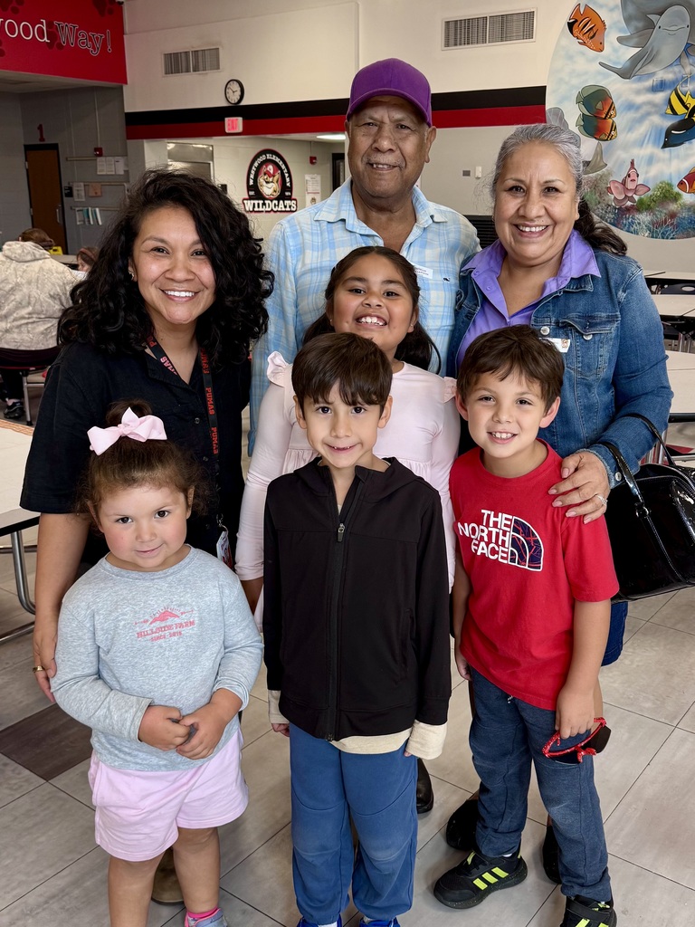 A group photo of six family members gathered in a school lobby with a colorful aquatic mural in the background. Two adults and four young children smile together for the camera.
