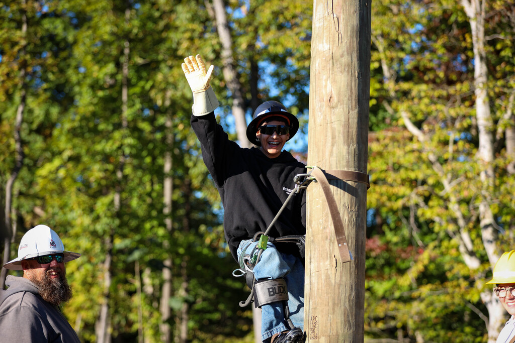 A student climbs a pole in lineman protective equipment.