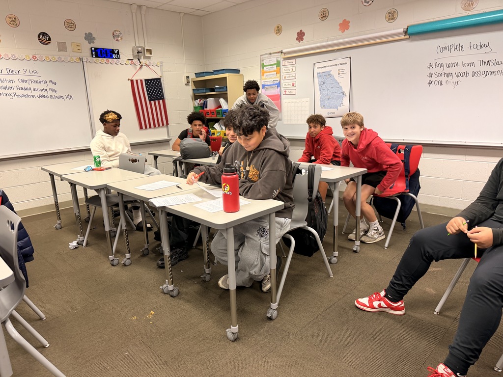 A group of middle school boys sitting at classroom desks reviewing debate notes and listening during class.