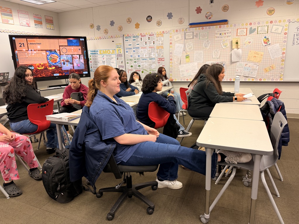 Middle school students seated at desks facing each other in a classroom during a structured debate activity with a digital timer displayed on the screen.