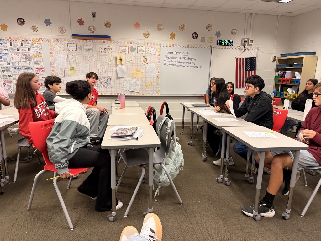 Middle school students participating in a classroom debate, seated across from one another at arranged desks.