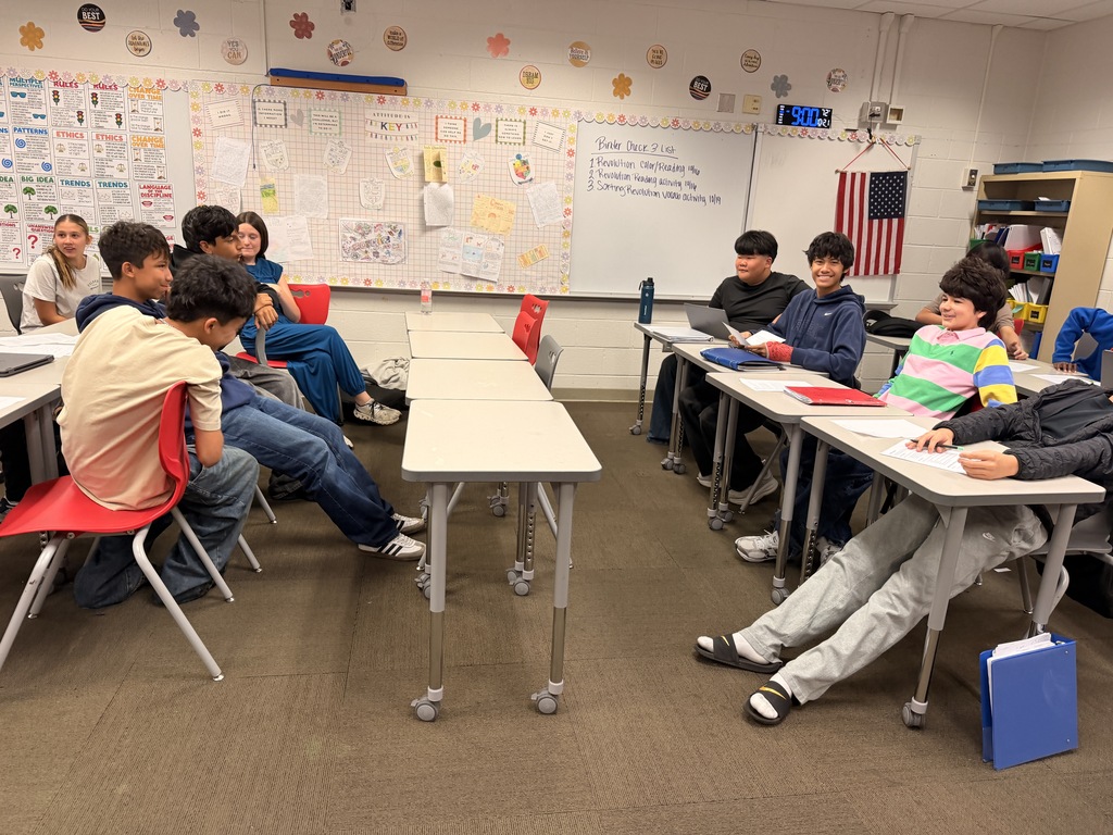 Students seated on opposing sides of classroom desks facing each other during a history debate.
