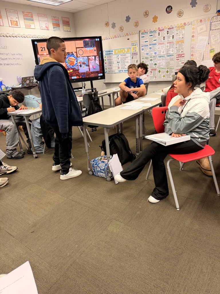 A student standing up to present an argument to classmates seated at desks during an in-class debate.