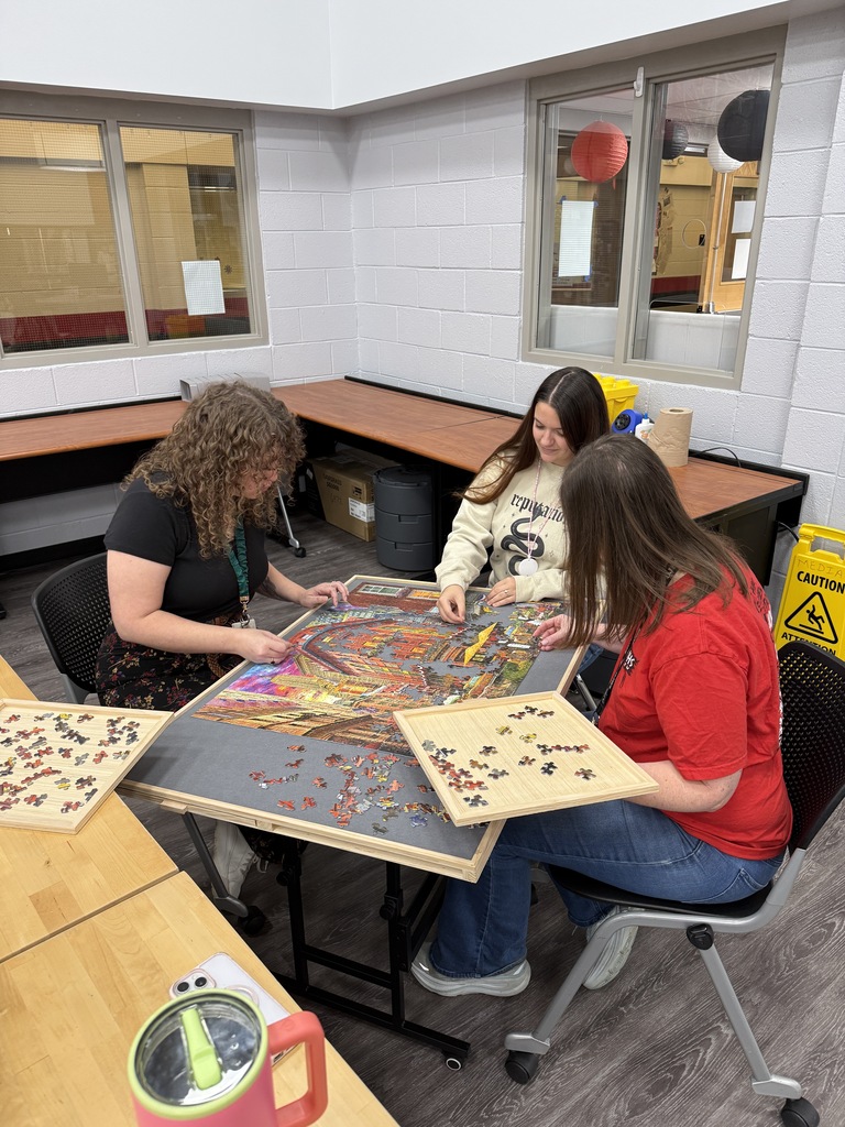 Three women sitting together around a tilted puzzle board assembling a colorful jigsaw puzzle using sorting trays.