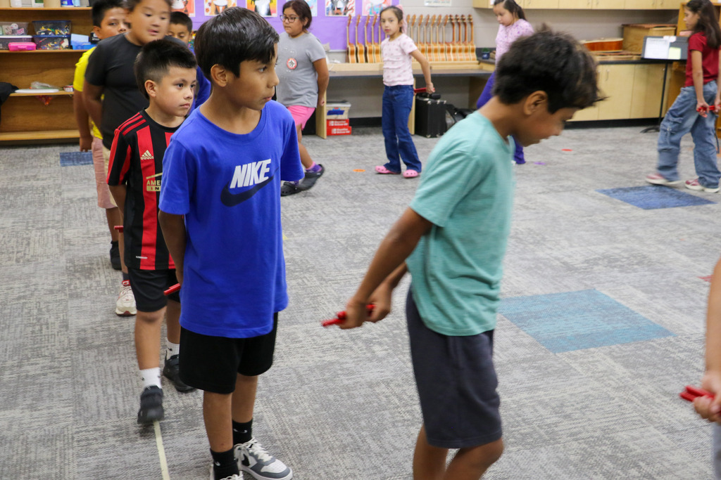 Students walk in a circle in their classroom while listening to music.