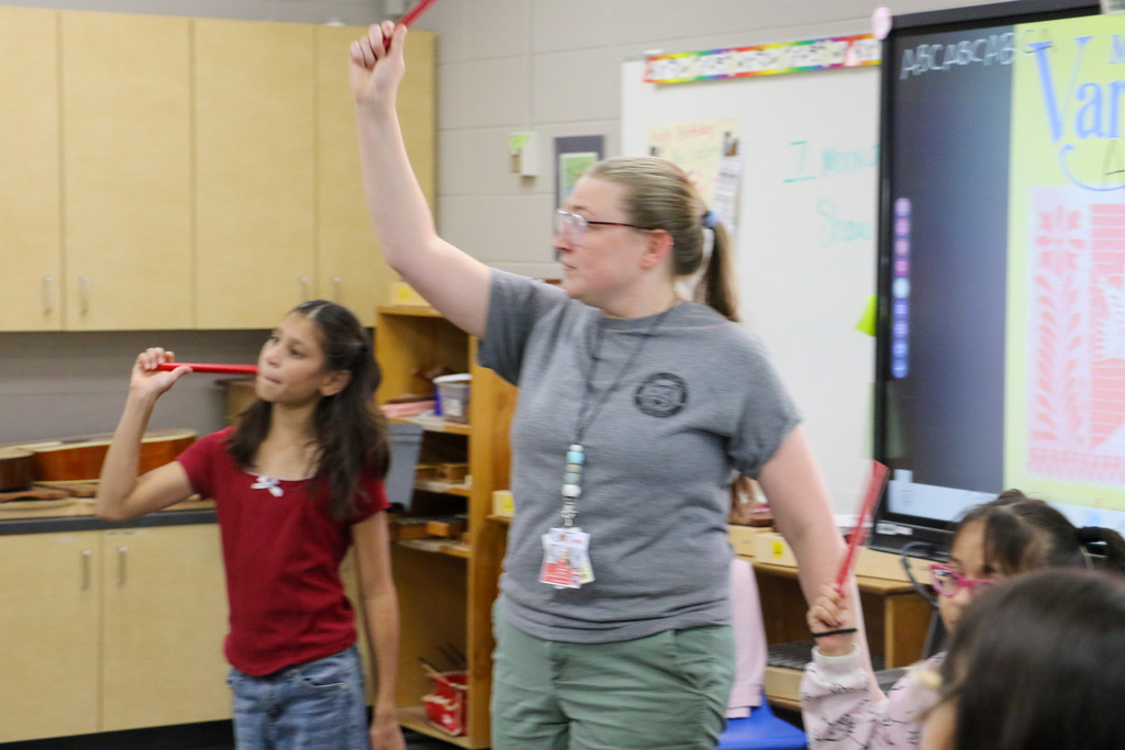 A teacher raises her drum stick into the air while marching.