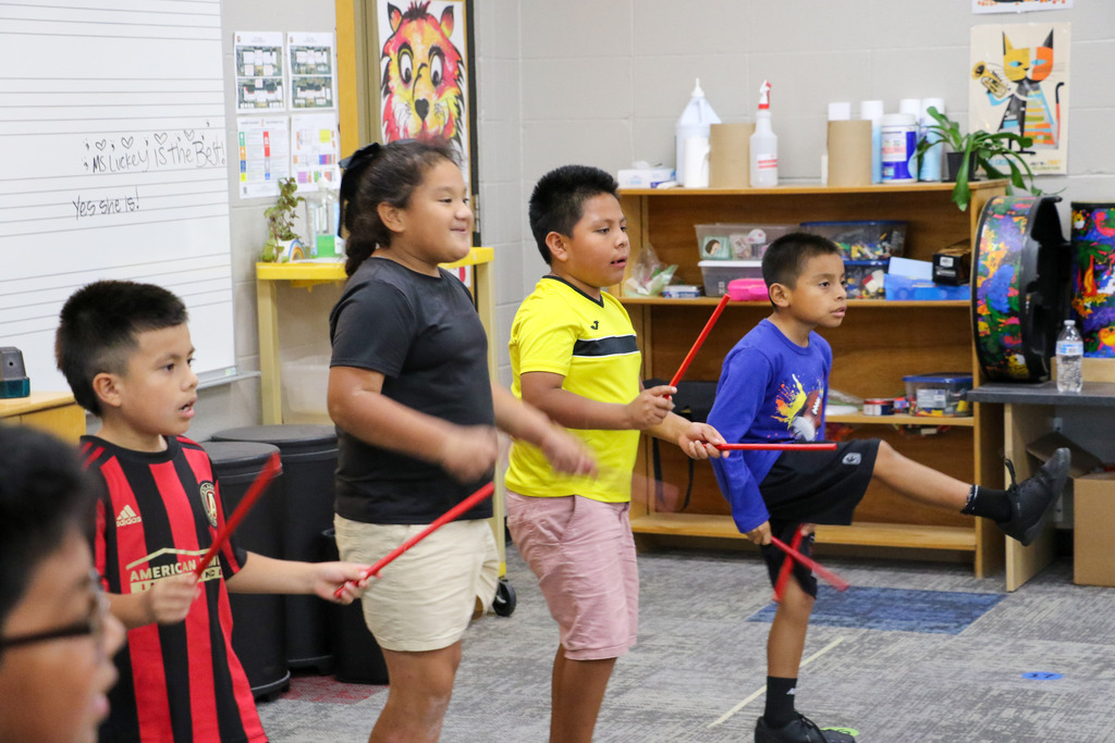 Students use sticks to keep time with the music.