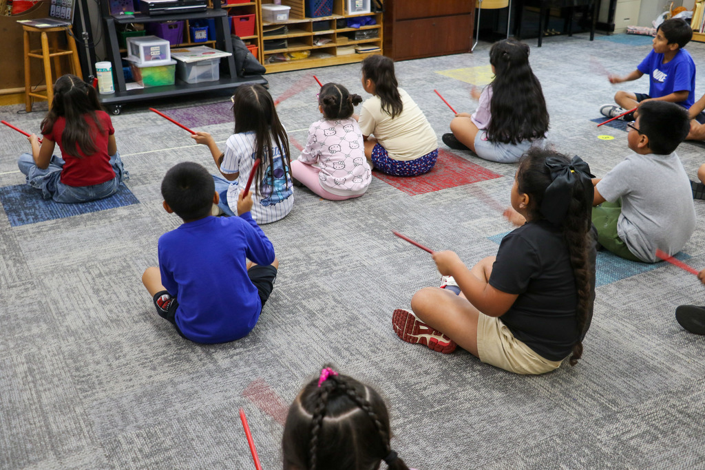 Studnets sit on a rug for music class.