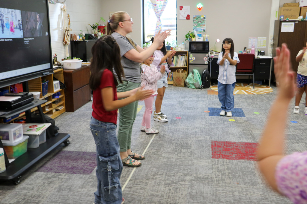 Students clap along with the music as their teacher instructs them.