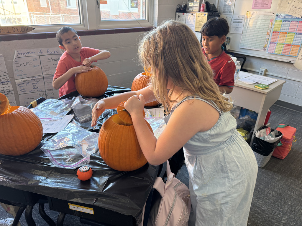 three students work at a table to carve their own pumpkins