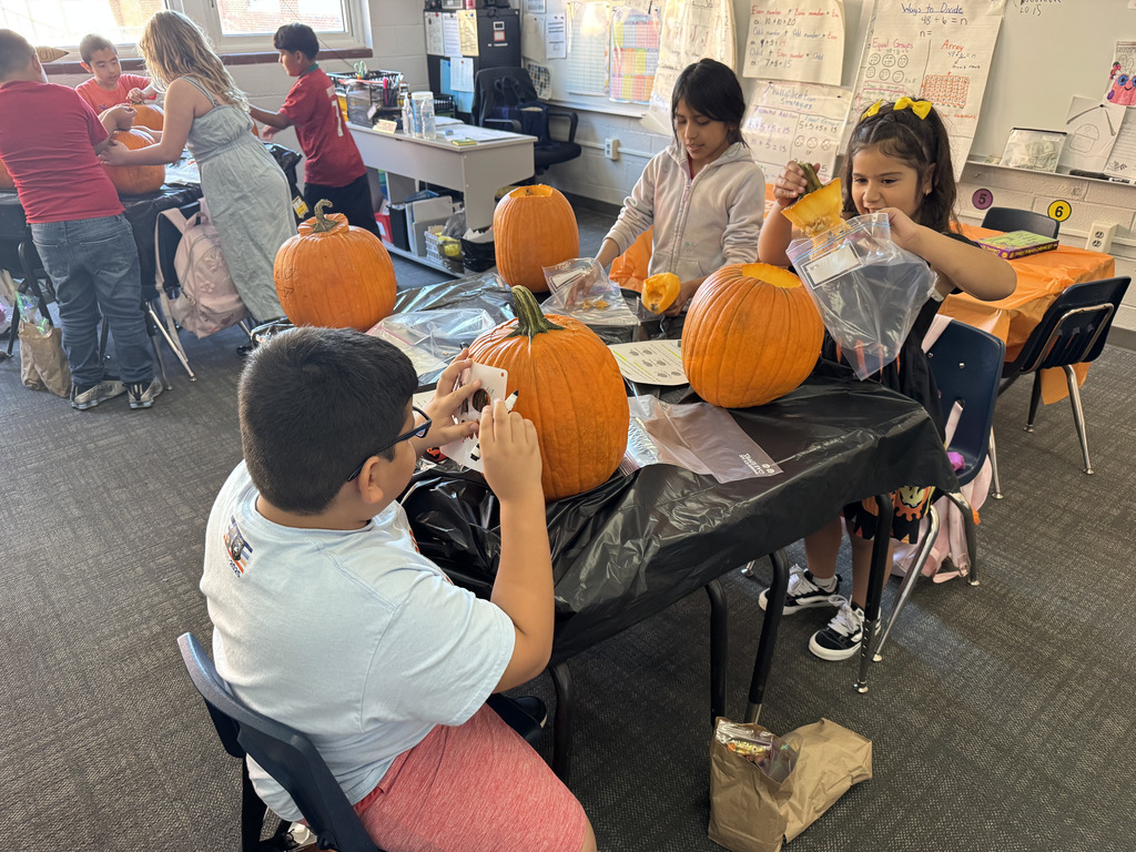 three students work at a table to carve their own pumpkins