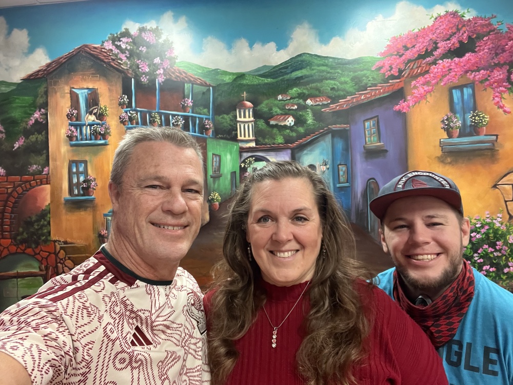 three people standing in front of a colorful mural