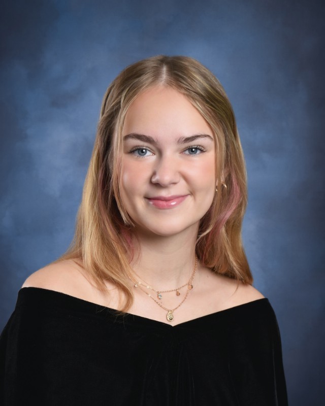 Senior portrait of Grace McCarthy with a blue background and wearing a black velvet dress.