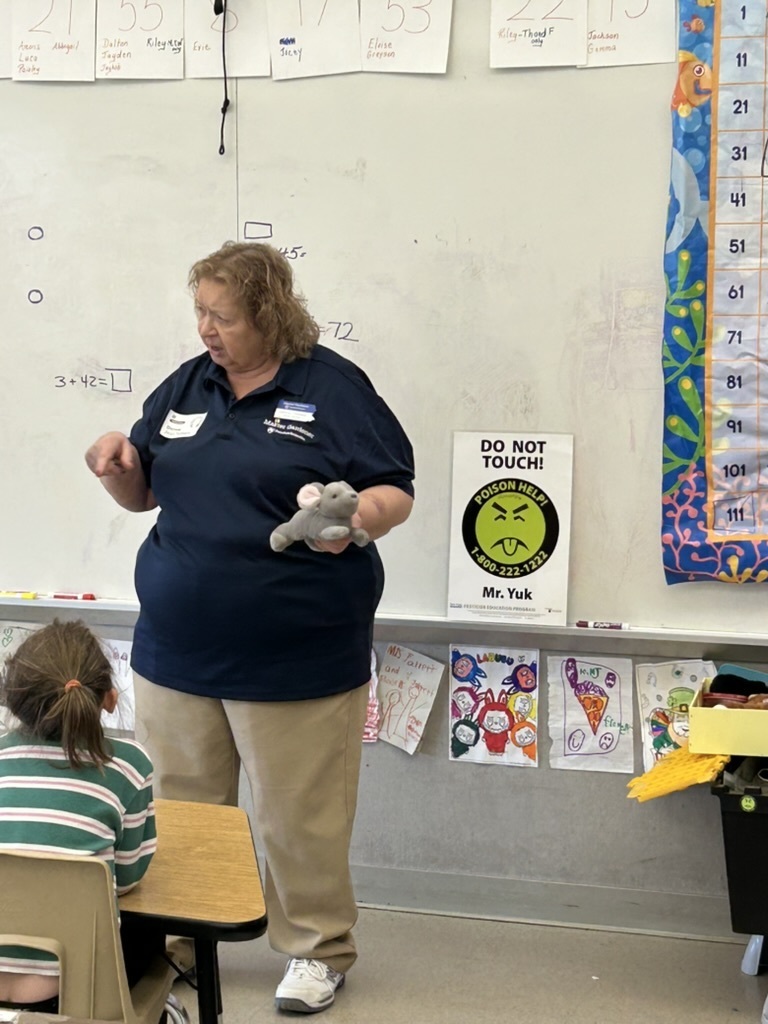 Penn State Master Gardener talking to students with a stuffed mouse and Mr. Yuck sticker in background.