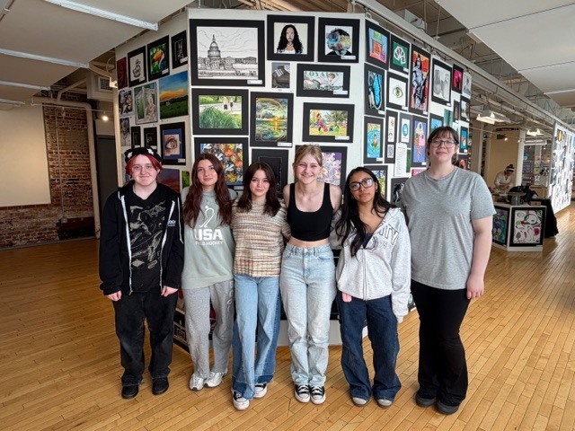 Six students standing in front of an art display at the Goggleworks