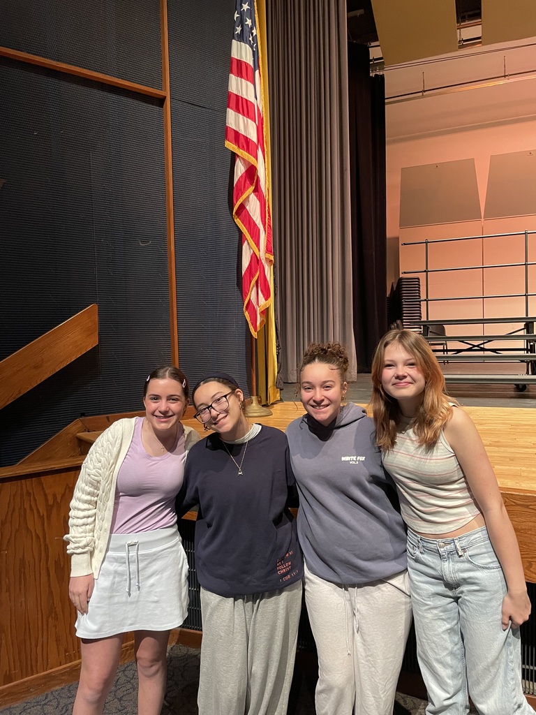 Four students standing in front of a stage with the American Flag in the background.
