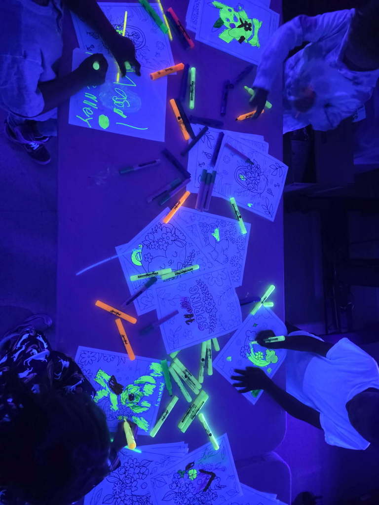 Picture of students using yellow and orange highlighters to color picture pages under blacklight.