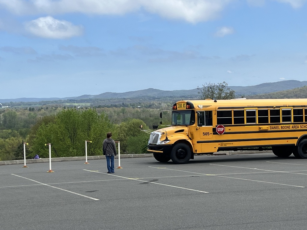 Bus driving in parking lot between pylons  with Monocacy Hill mountain in background.