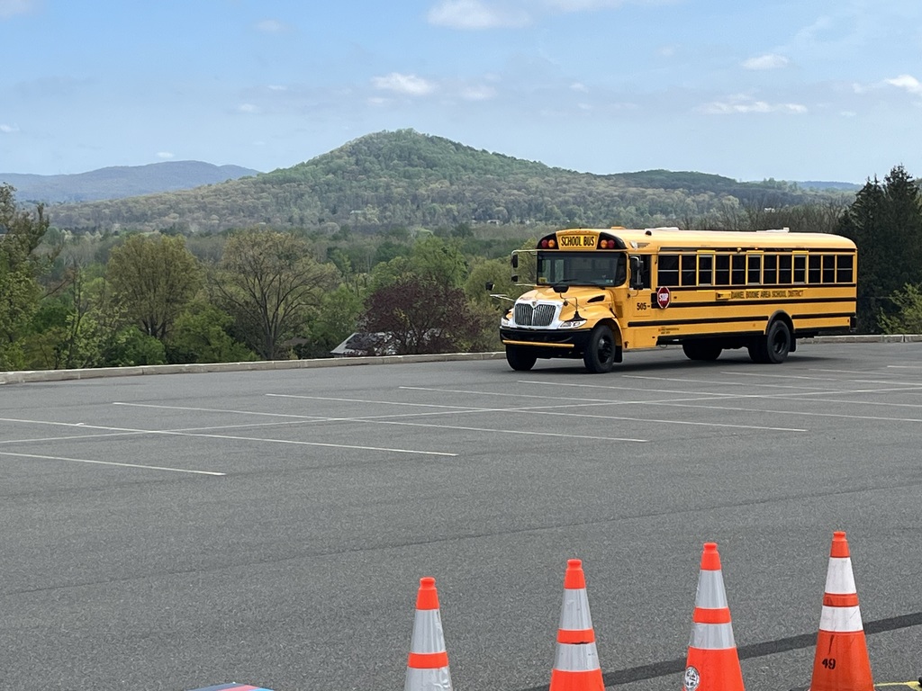 Bus driving in parking lot with four orange cones in forefront and Monocacy Hill mountain in background.