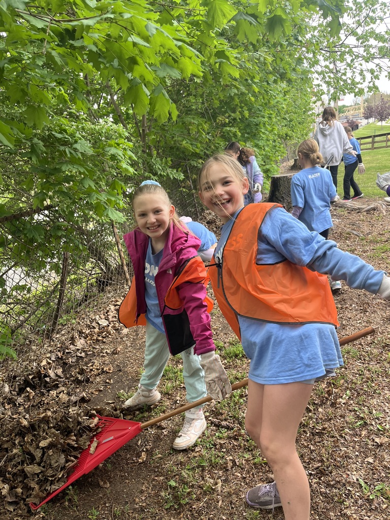Two students using a rake to pickup leaves