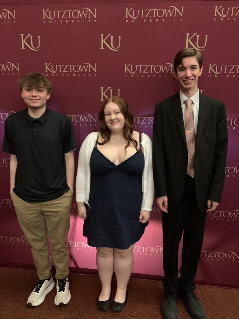 Three students standing in front of a Kutztown University maroon & gold step and repeat sign.