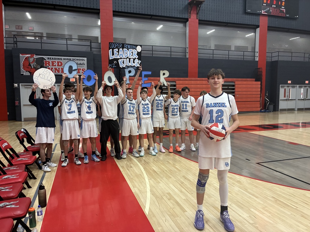 Photo of 12 students standing behind Cooper Robison in a school gym. Students are on the volleyball team dressed in Daniel Boone uniforms. They  are holding signs that read  739 Kills School Record, Cooper Robison Leader in Kills @DBAHS #12 and large letters cut out to spell COOPER. Cooper is standing in the foreground holding a red white and blue volleyball with the date 4/30/26  vs. Reading