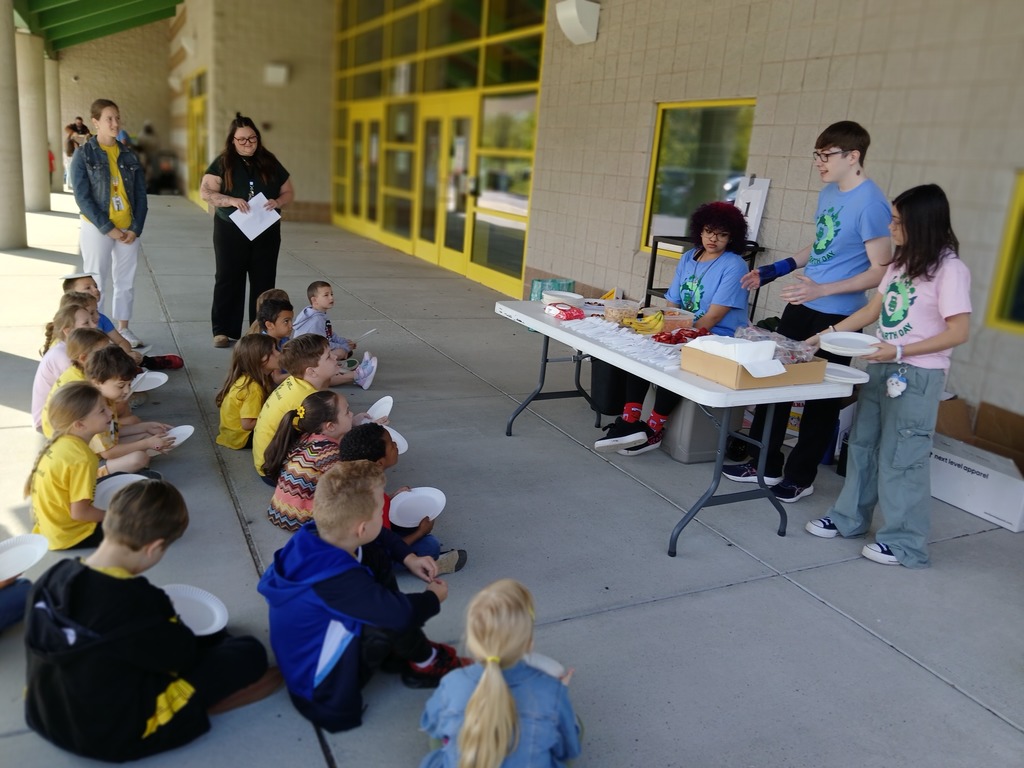 Students sitting on sidewalk listening to three high school students from the Ecology Club.
