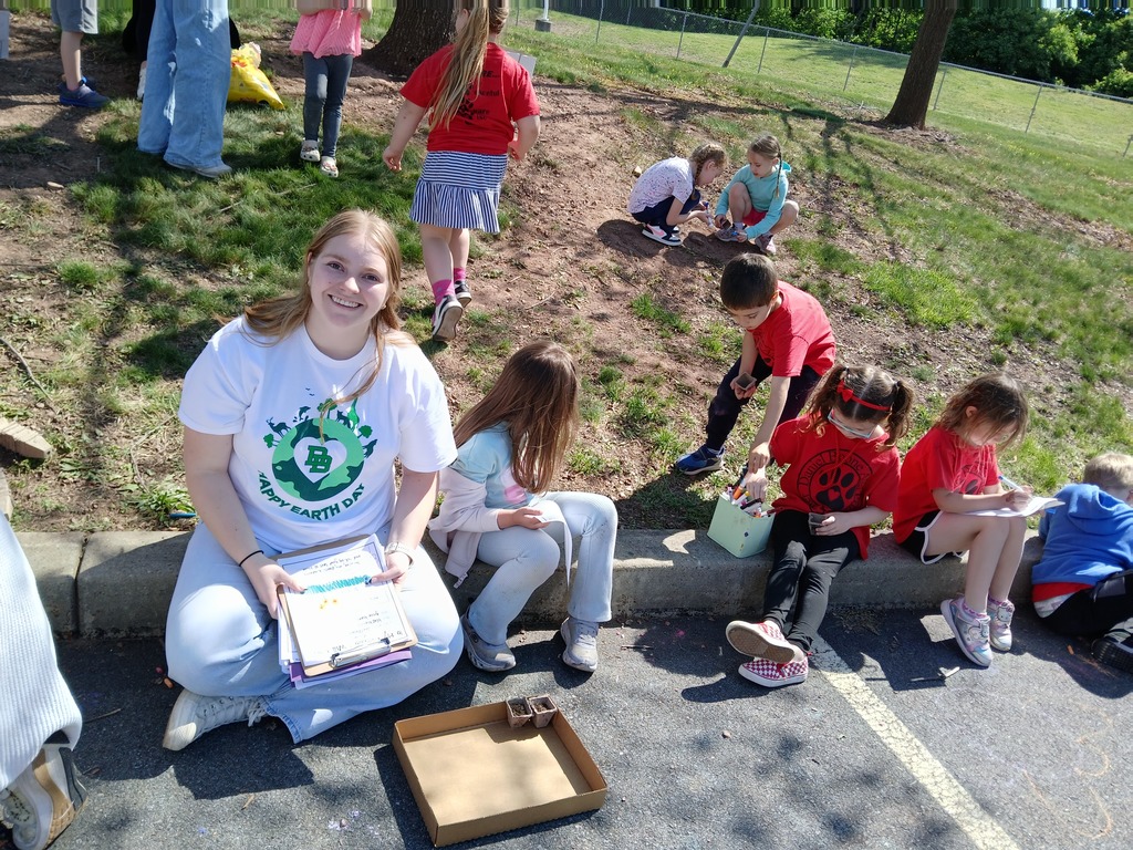 High school student smiling at camera while four kindergarteners work on planting and writing.