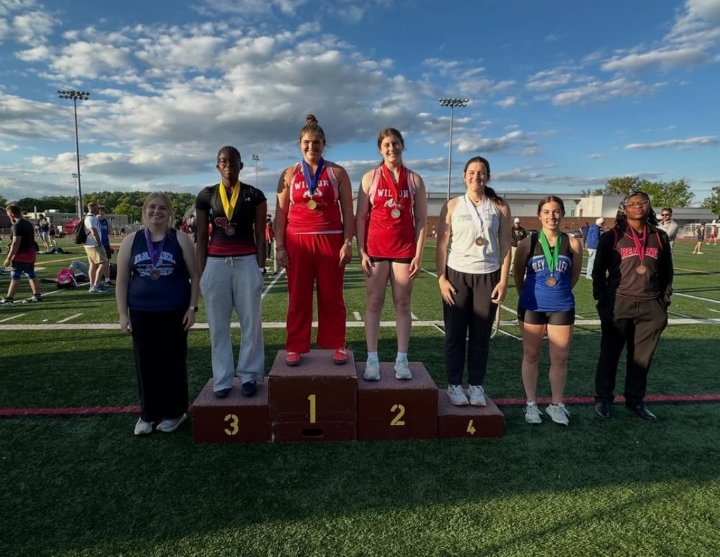 Seven students standing on a football field on risers wearing medals.