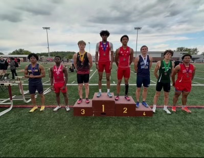 Eight students standing on the football field wearing medals.
