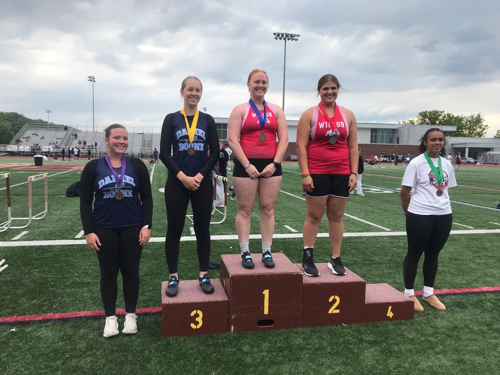 Picture of 5 girls standing on podium with medals on a football field.