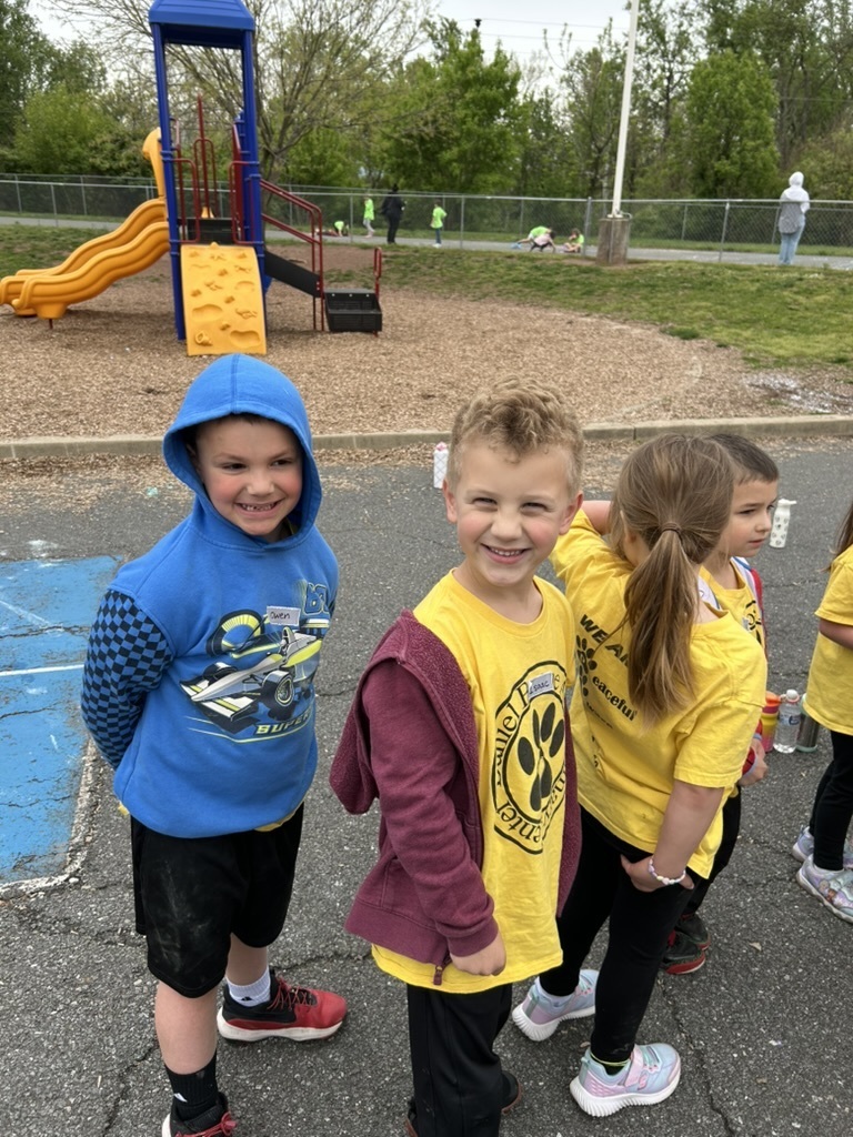 A picture of students waiting in line on the playground. Two students are smiling at the camera while the other two are waiting patiently. 