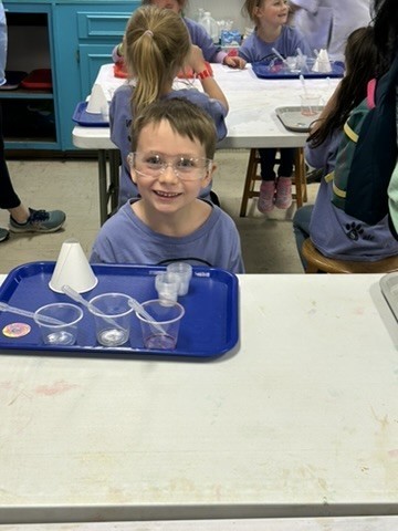 Picture of a student sitting in front of a tray with three plastic cups with droppers, a paper cone and smaller plastic 1 oz cups.